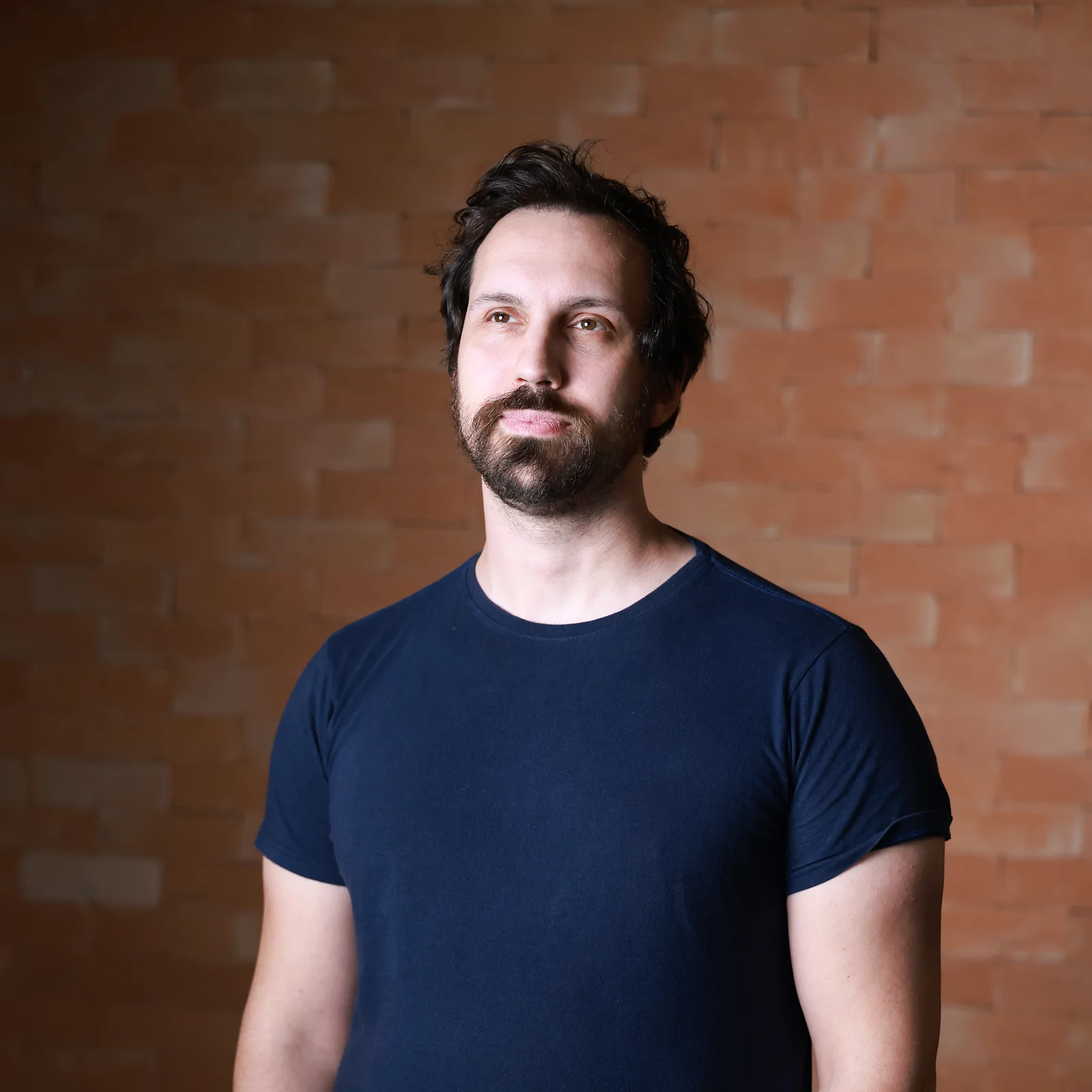 Felipe Fiori, psicanalista, de pé diante de uma parede de tijolos.